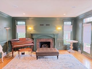 A living room with green walls , a fireplace , a piano and an ottoman.