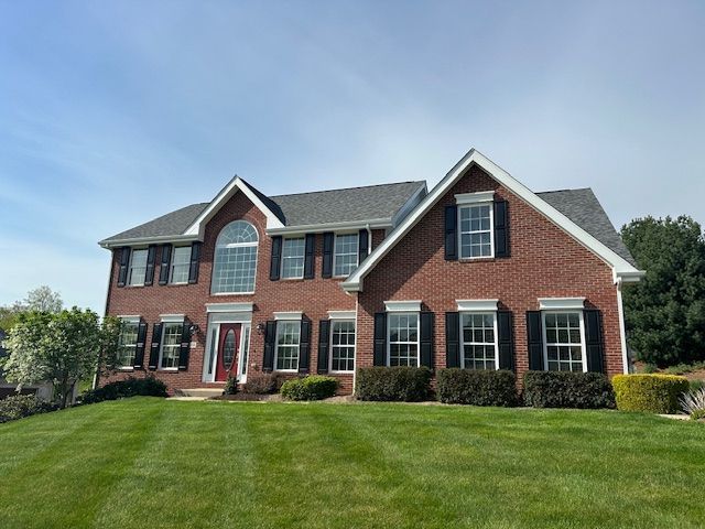 A large brick house with black shutters and a lush green lawn