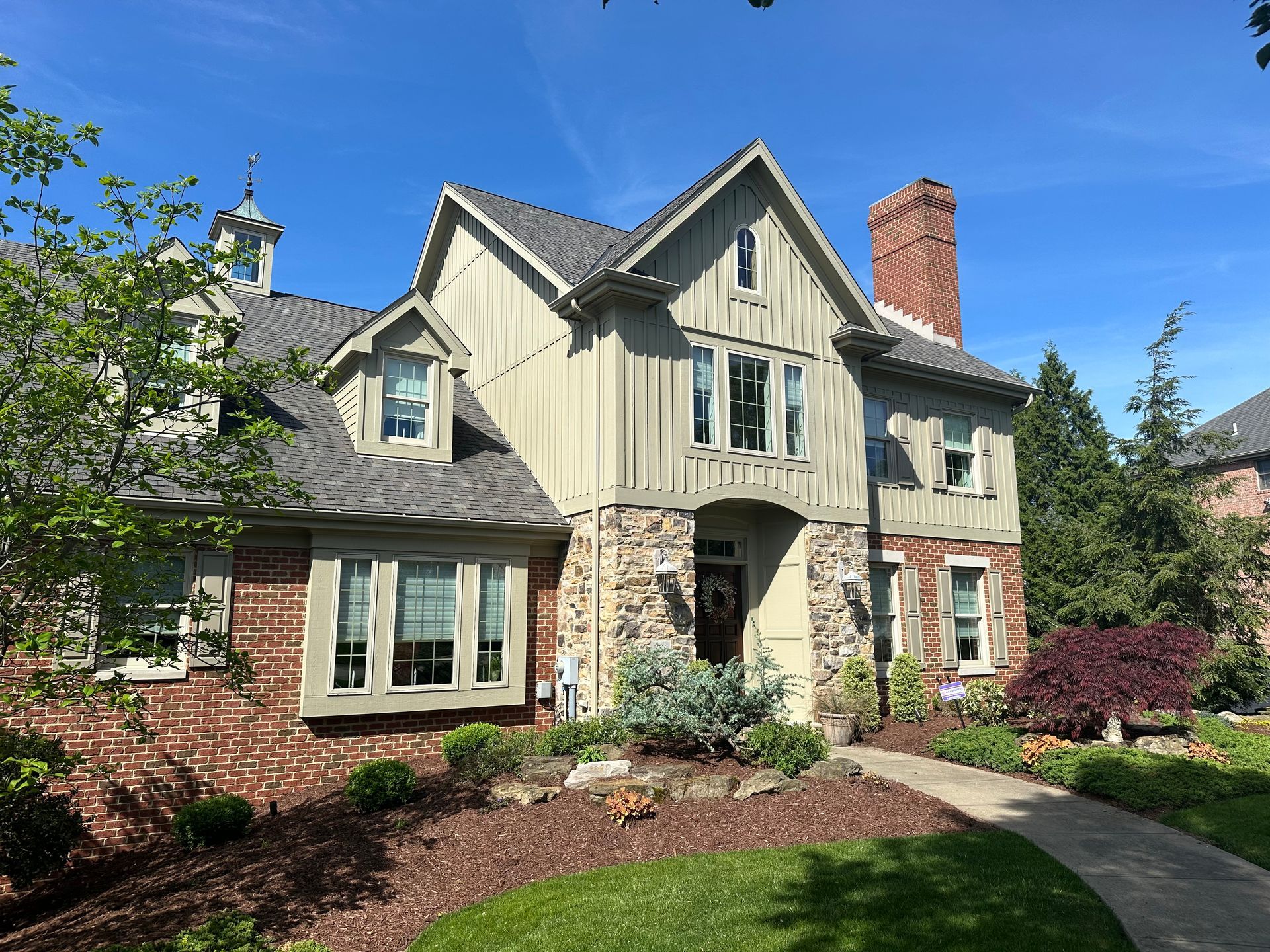 A large brick house with a gray roof and a walkway leading to it.