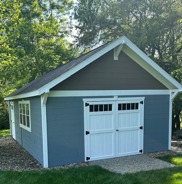 A blue garage with white doors is surrounded by trees