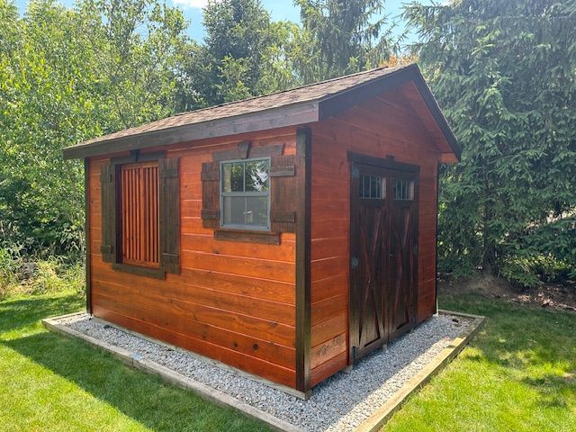 A wooden shed with a window and shutters is sitting in the middle of a lush green field.