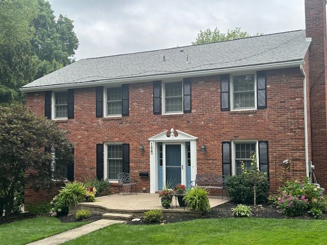 A large brick house with a gray roof and black shutters.