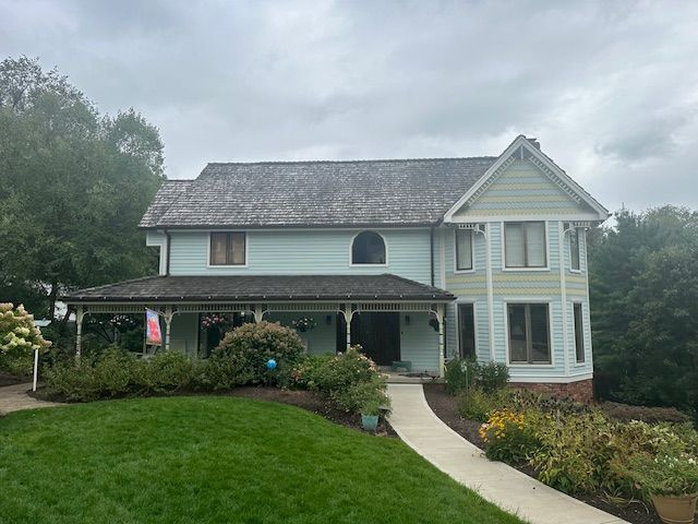 A large white house with a gray roof and a large lawn in front of it.