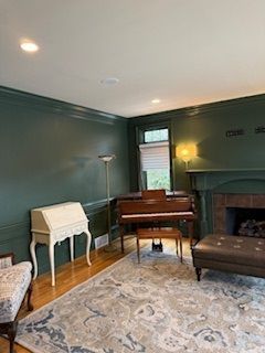 A living room with green walls , a piano , a fireplace and a rug.