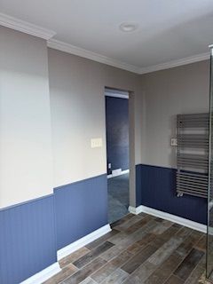 A bathroom with blue walls , wooden floors , and a towel rack.