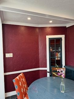 A dining room with a table and chairs and a vase of flowers on the table.