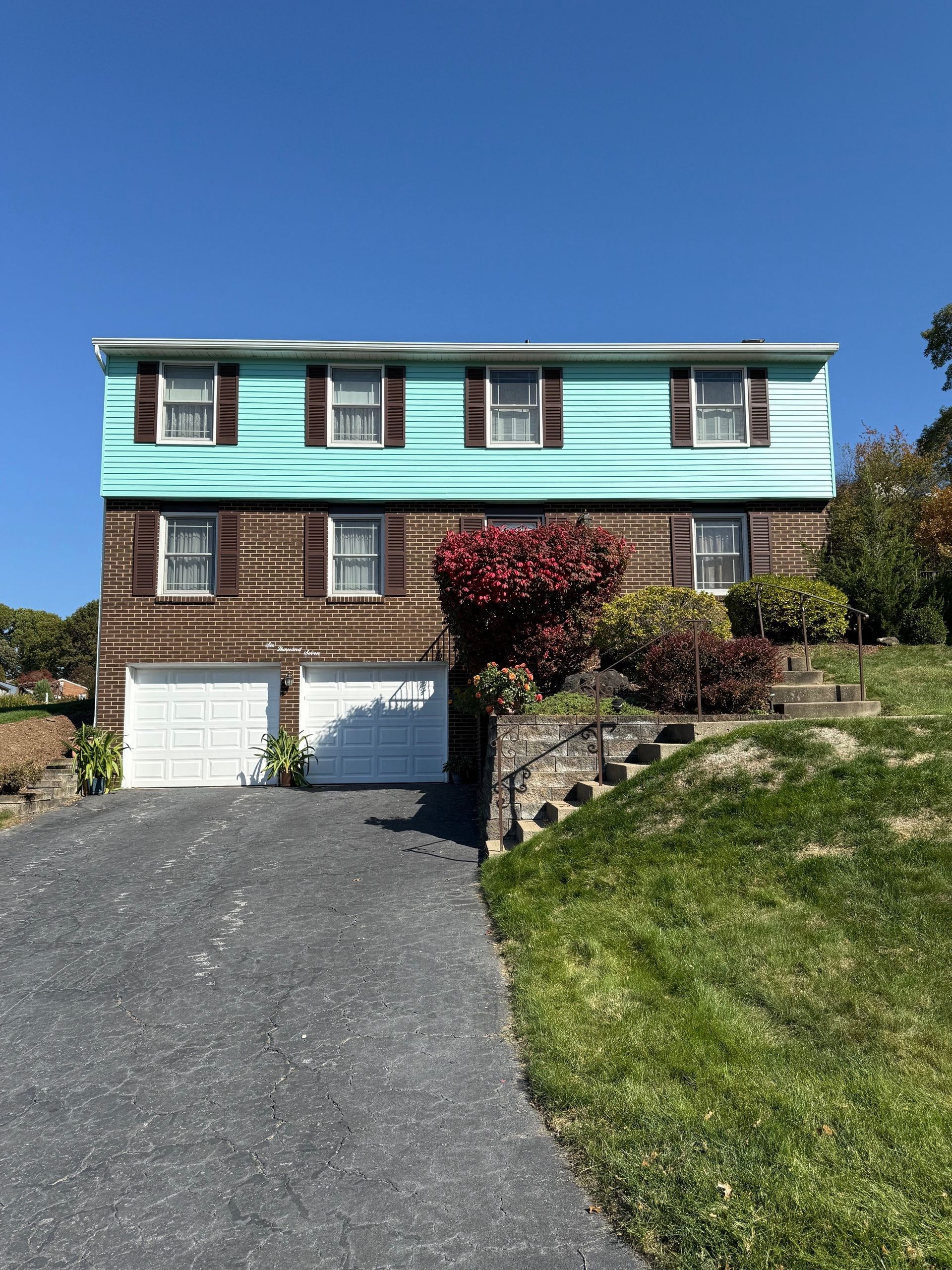 A house with a blue siding and brown shutters is sitting on top of a hill.