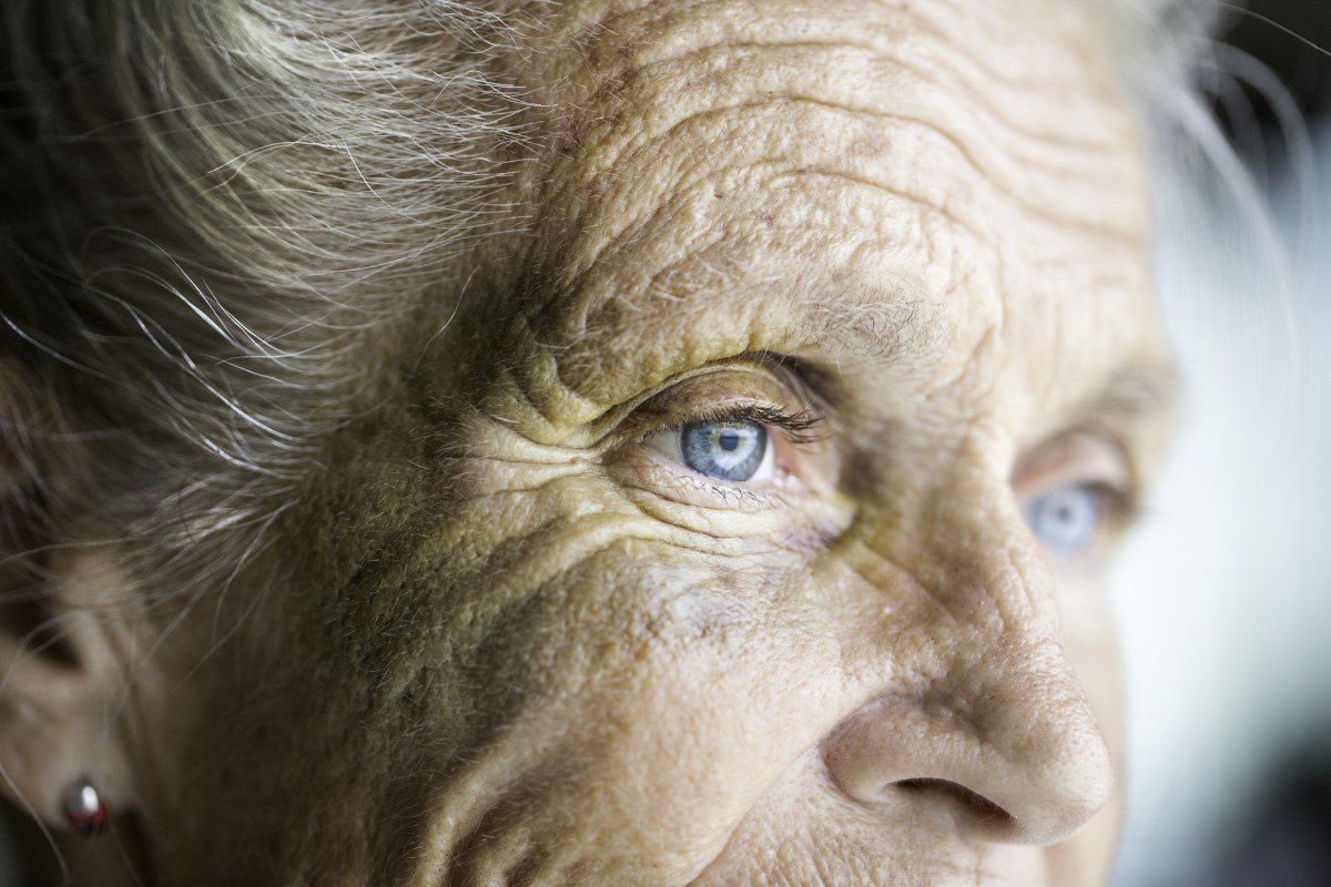 Close-up of a wrinkled face with blue eyes, softly lit from the side.