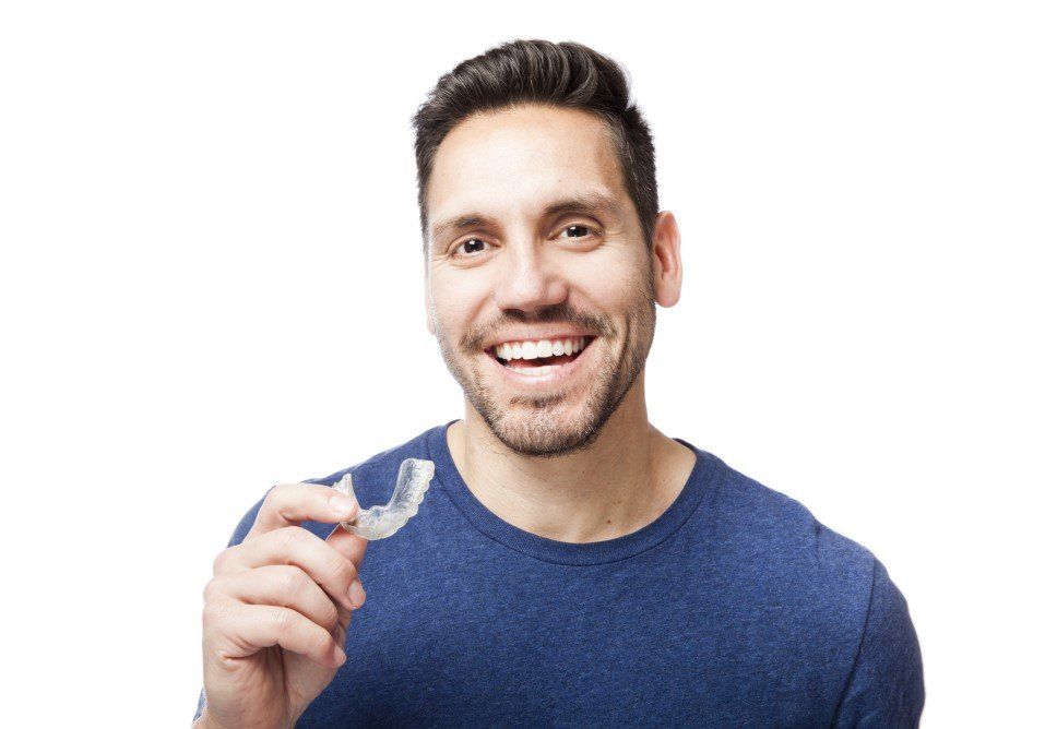 Smiling man in a blue shirt holding a clear dental aligner against a white background