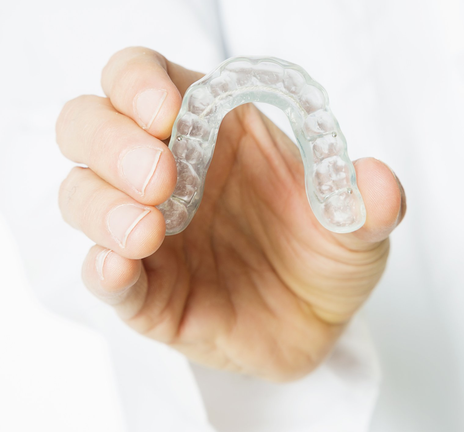 Hand holding a clear plastic dental aligner against a white background