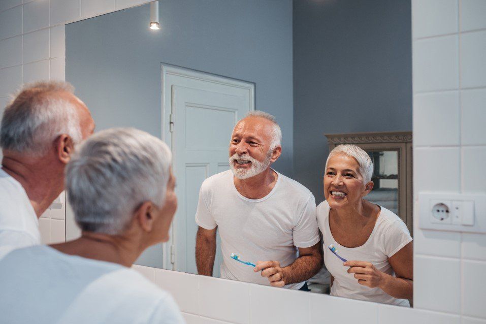 Old couple smiling on the mirror while brushing teeth