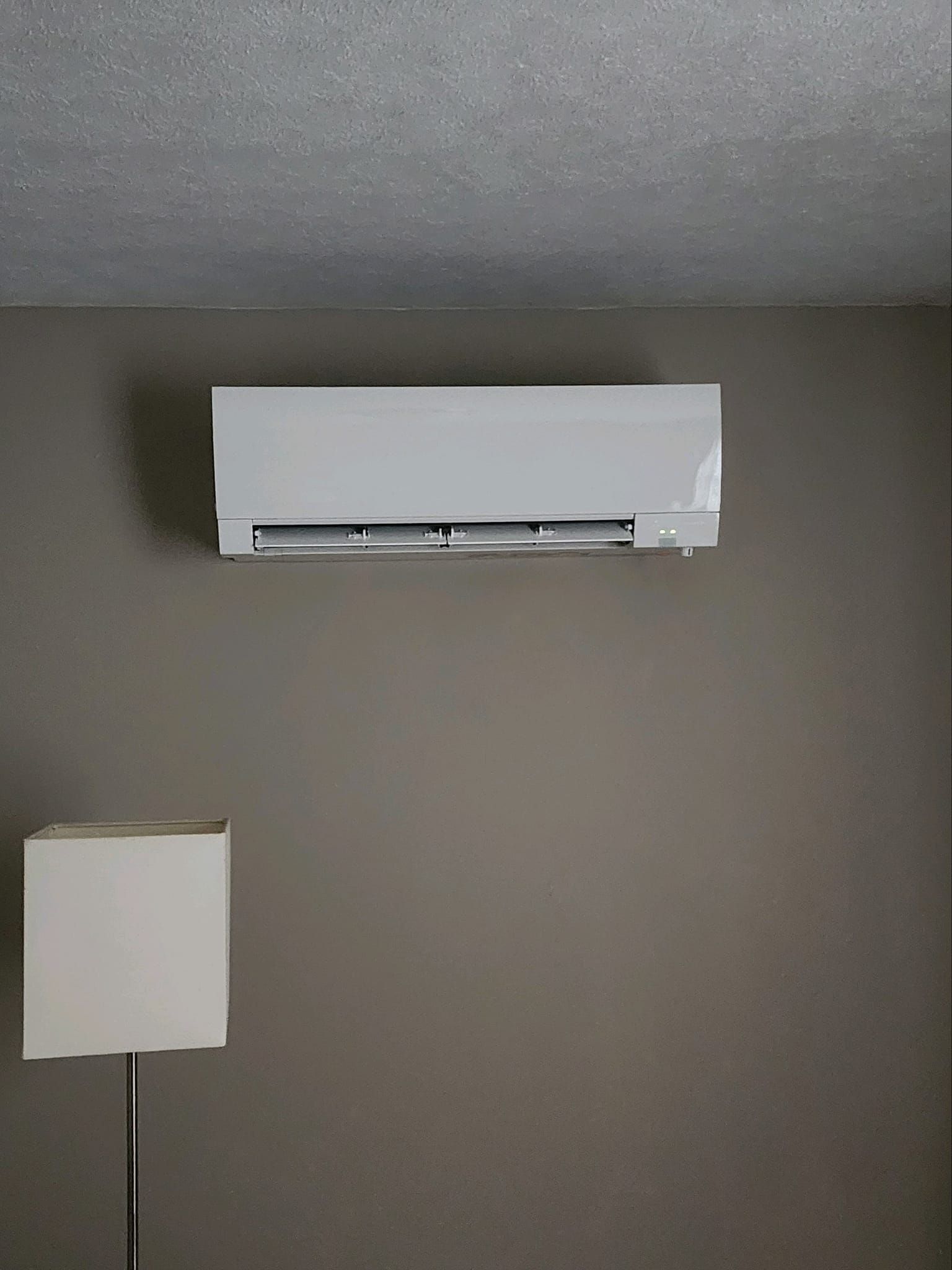 A white air conditioner is hanging from the ceiling in a room.