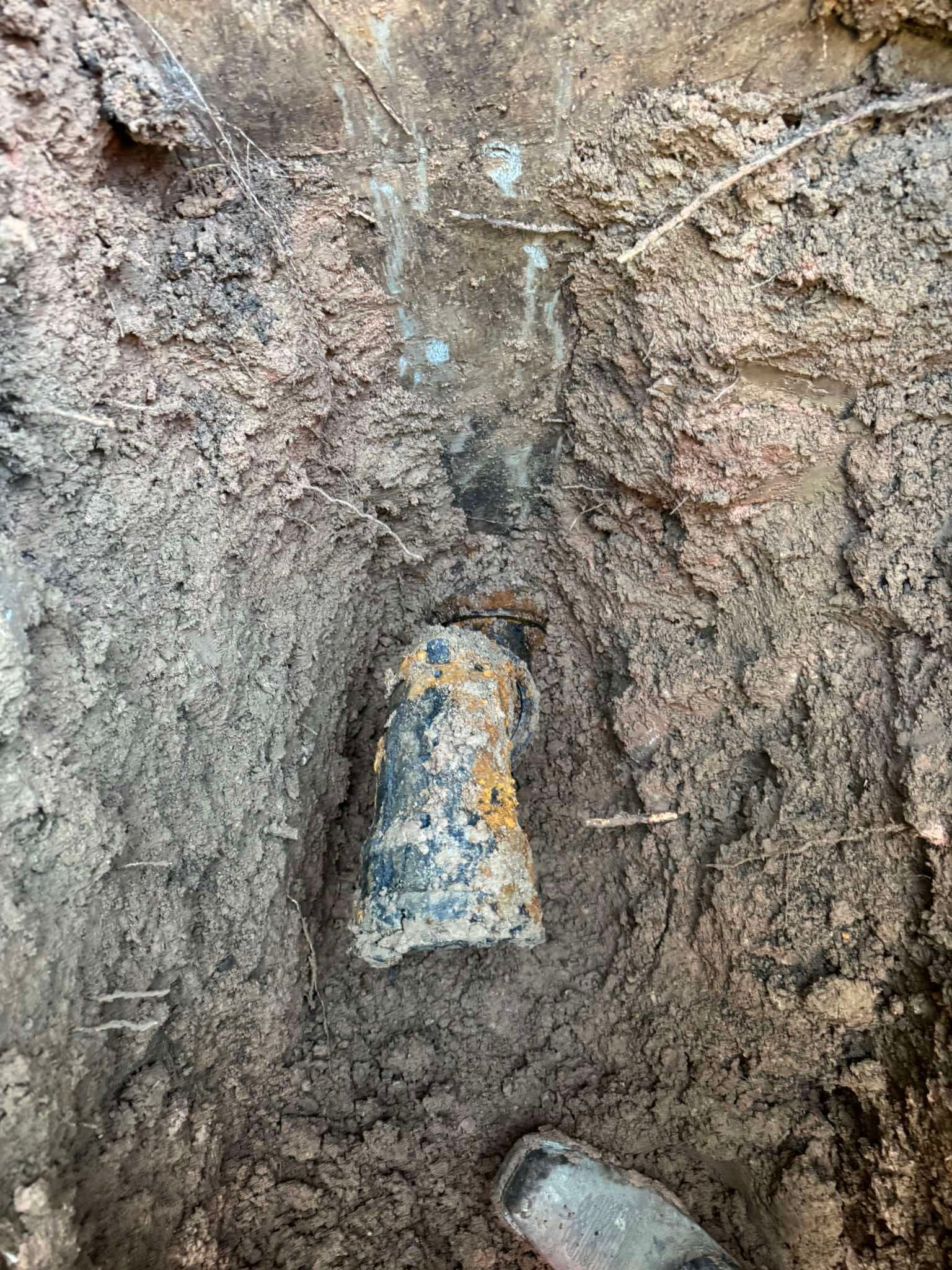 A close-up view of a rusted, cylindrical pipe embedded in dark, damp soil.