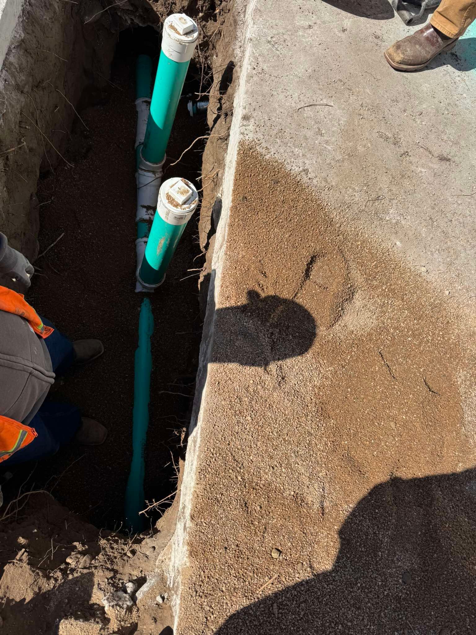 Workers in a trench installing green PVC pipes next to a concrete curb.