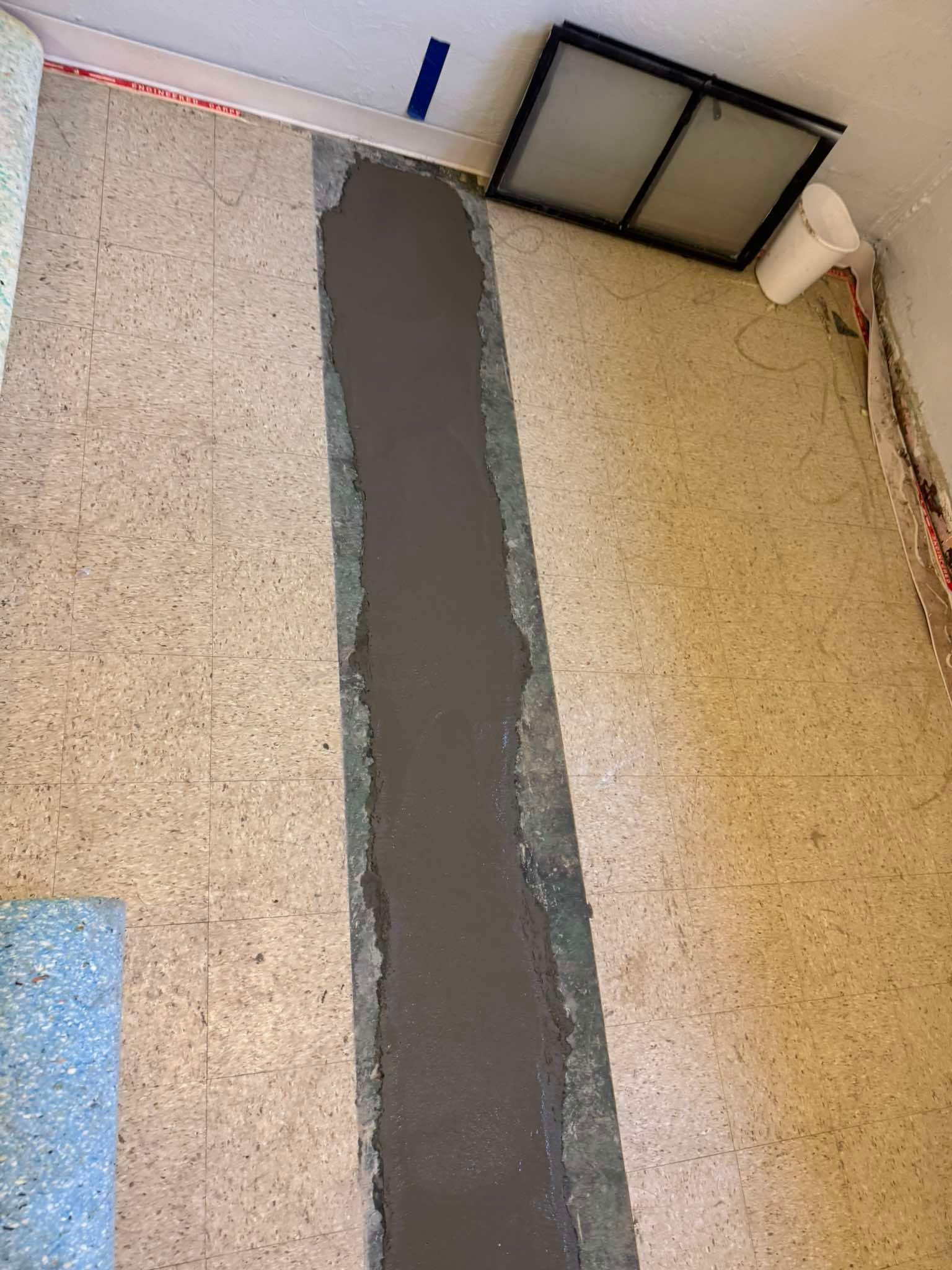 A floor with a long, vertical trench filled with smooth gray concrete, flanked by mottled beige square tiles.