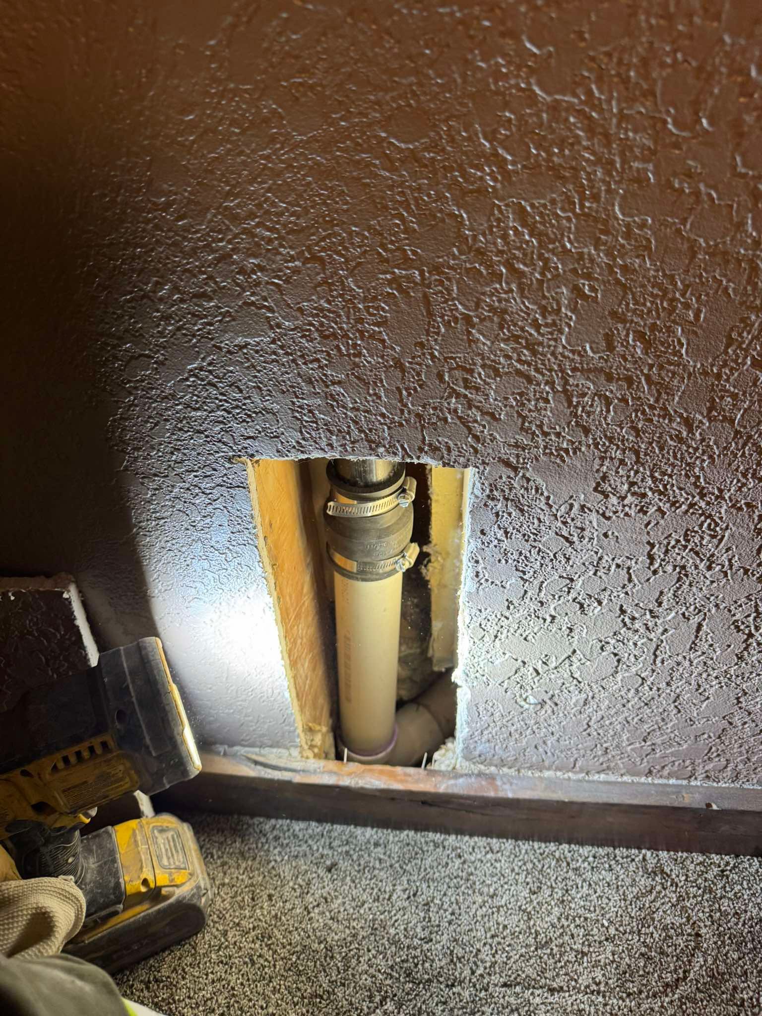 A vertical pipe connected with a rubber coupling inside a rectangular hole cut into a textured, brown wall.
