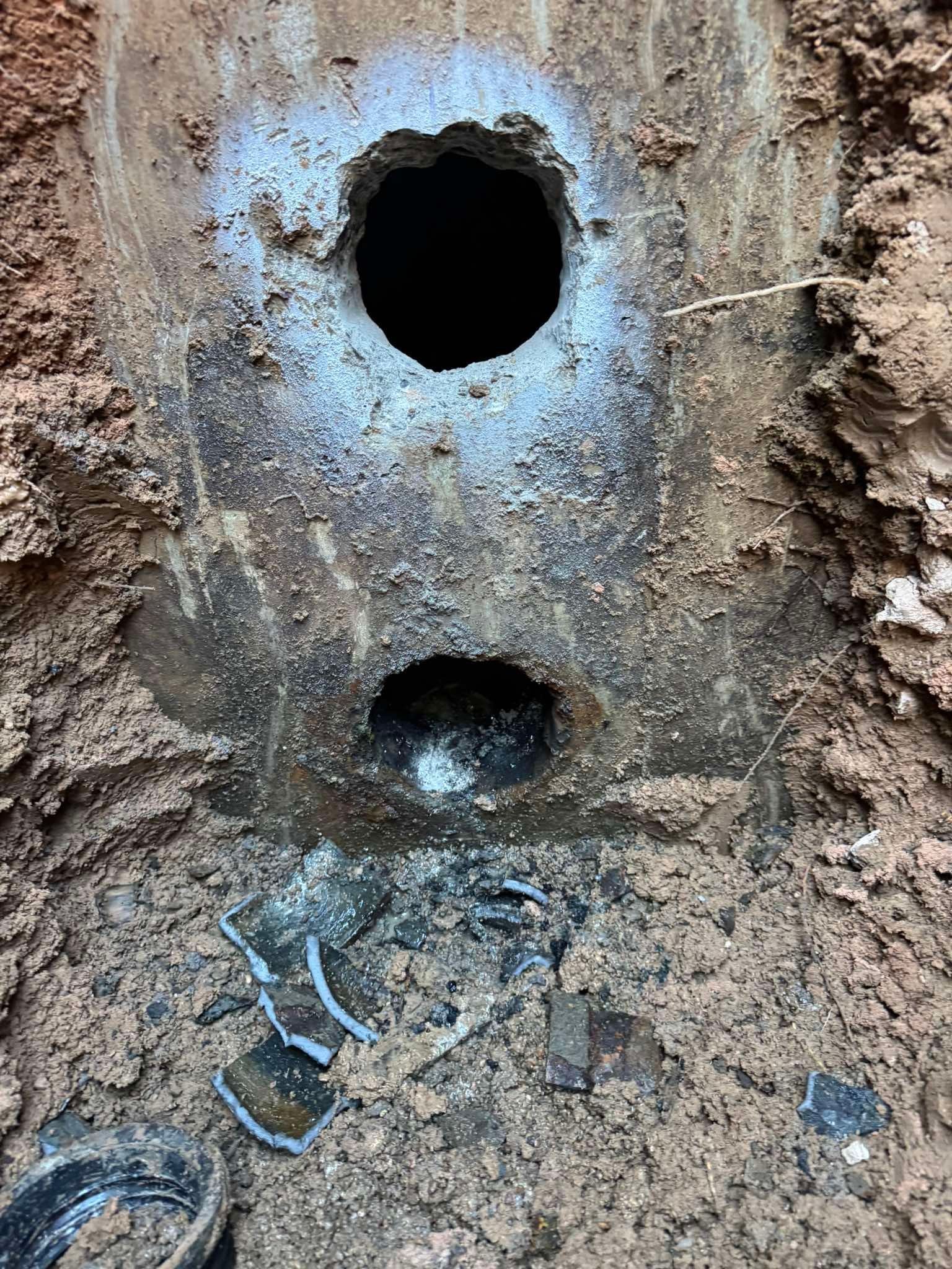 A close-up view of two circular holes in a dark, concrete pipe structure set within moist, excavated dirt.