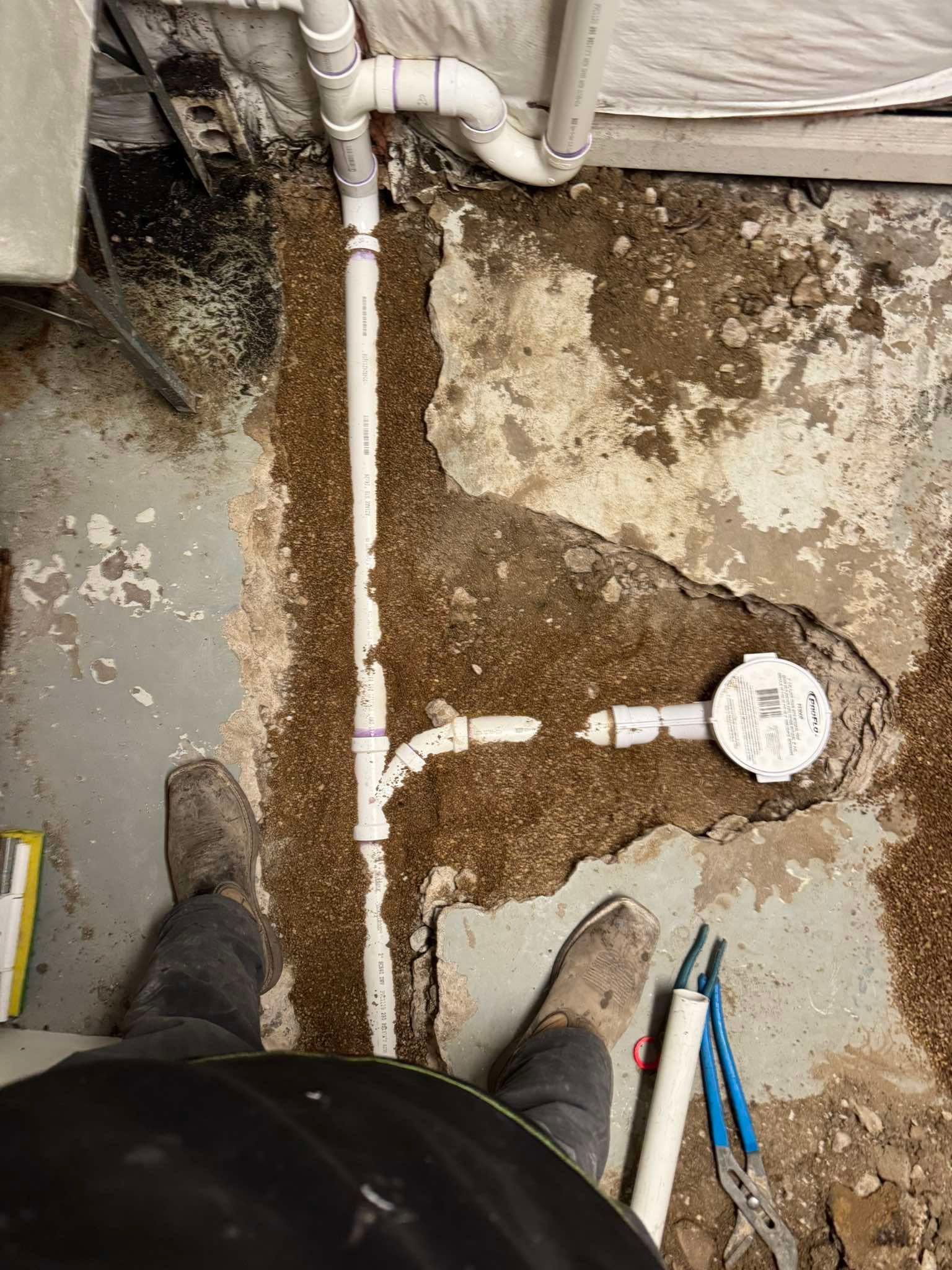 New white PVC plumbing pipes installed in a narrow trench cut through a concrete basement floor.