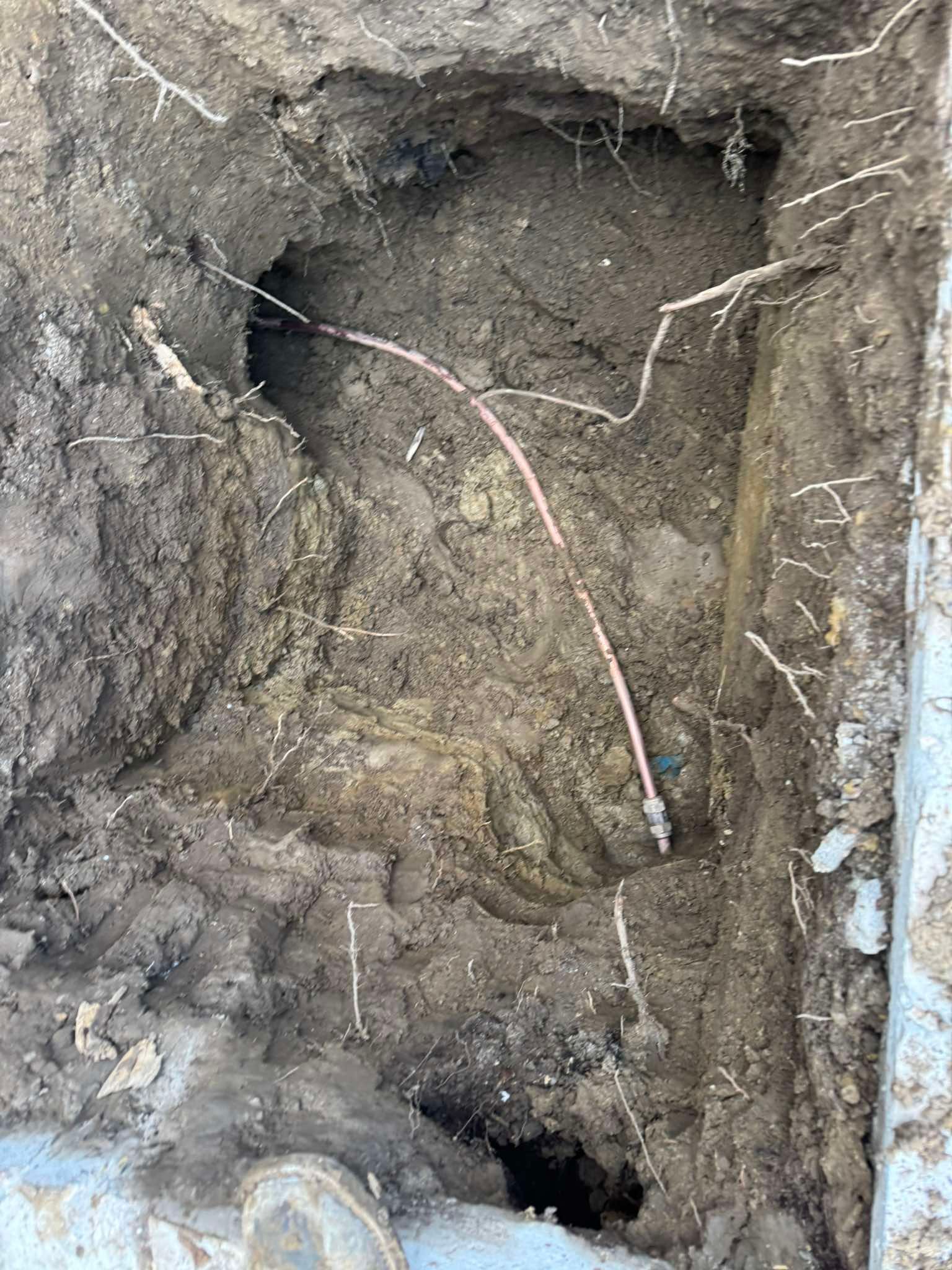 A trench dug into the dirt shows a single exposed copper wire extending across the center.