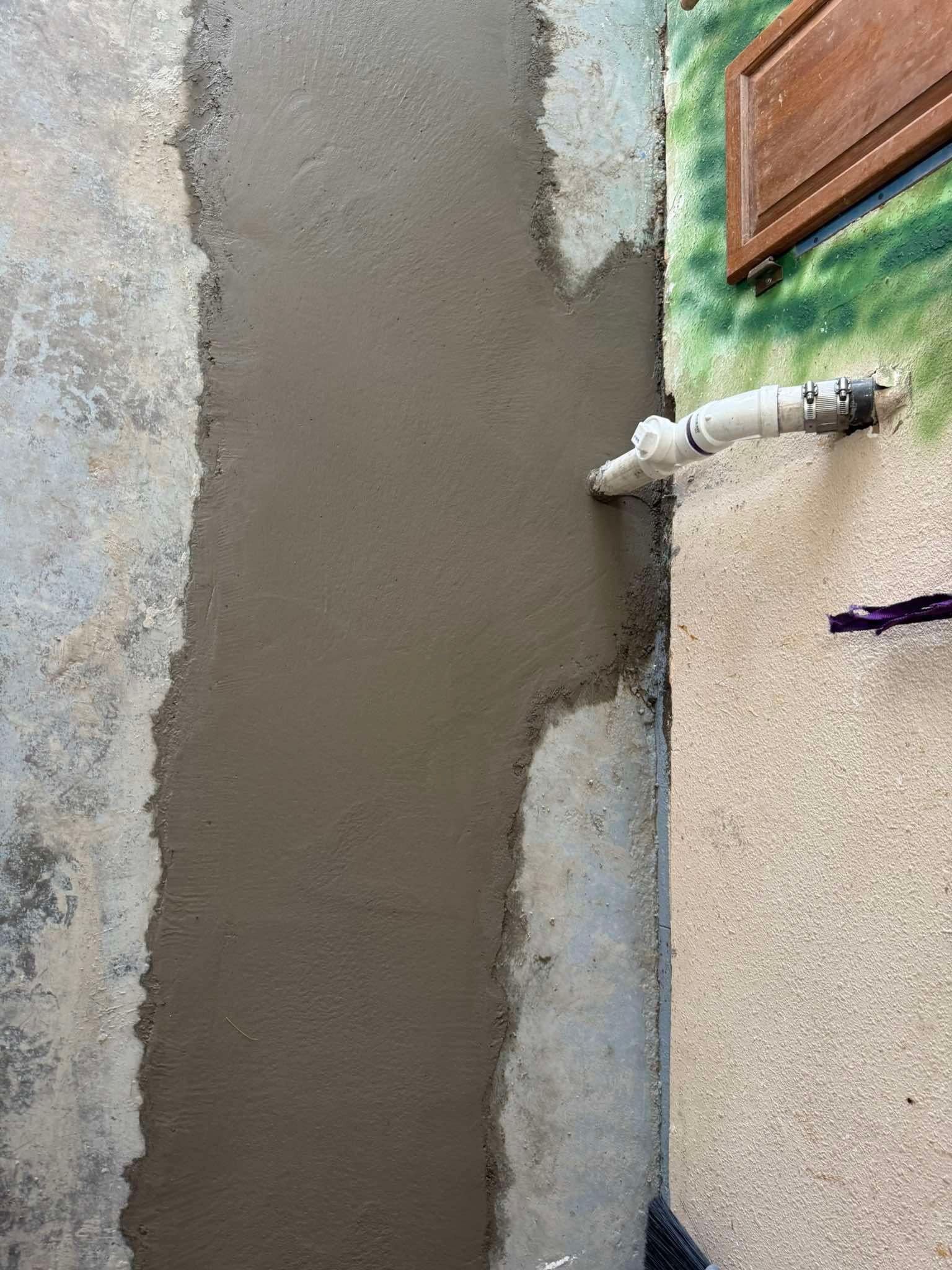 A narrow trench filled with fresh, wet gray concrete along an interior wall near a white plumbing pipe.