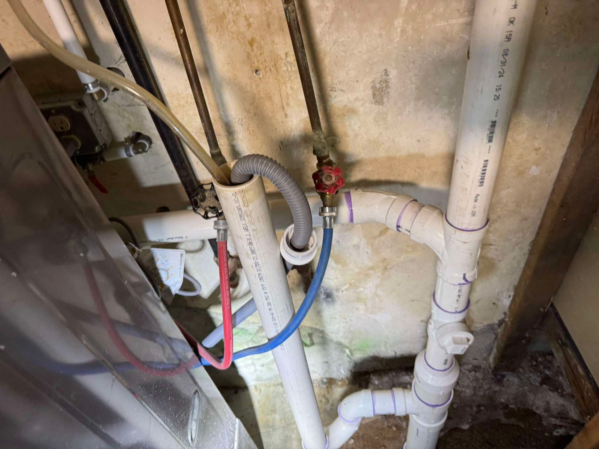 A water heater setup with plumbing pipes, valves, and a drainage line connected to white PVC drainage piping.