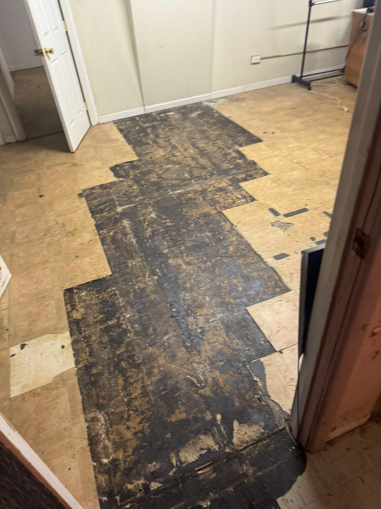 An interior room floor shows a central path of exposed, dark, sticky subflooring amidst light-colored floor tiles.
