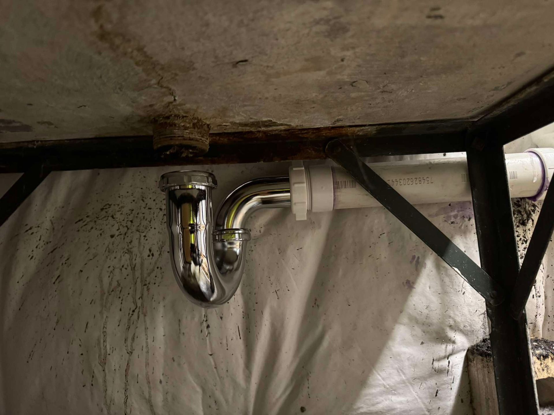 A detached metal P-trap pipe hanging beneath a sink drain, not connected to the plumbing above.
