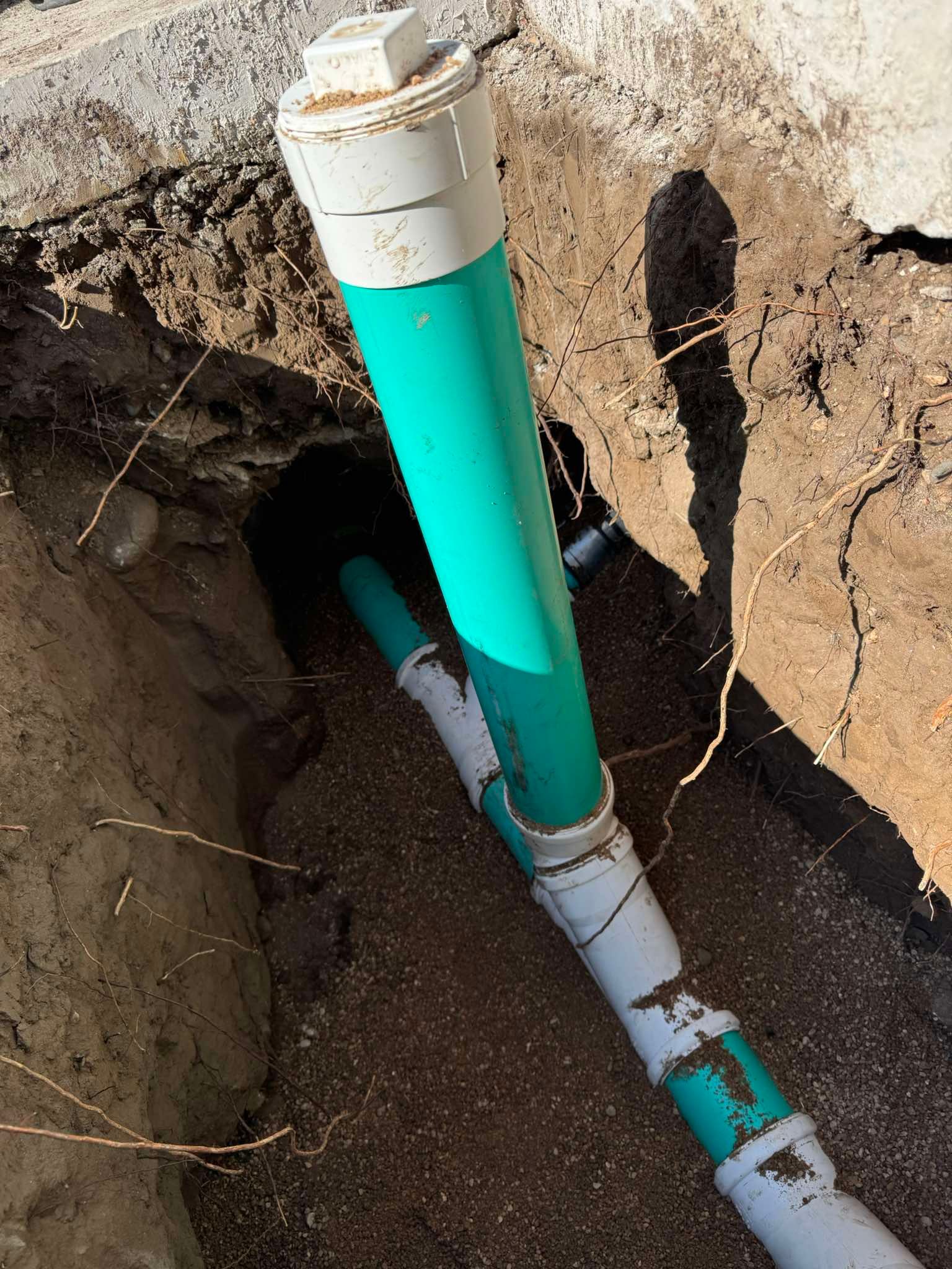 Green and white PVC pipe assembly installed in an open dirt trench for sewer or drainage access.