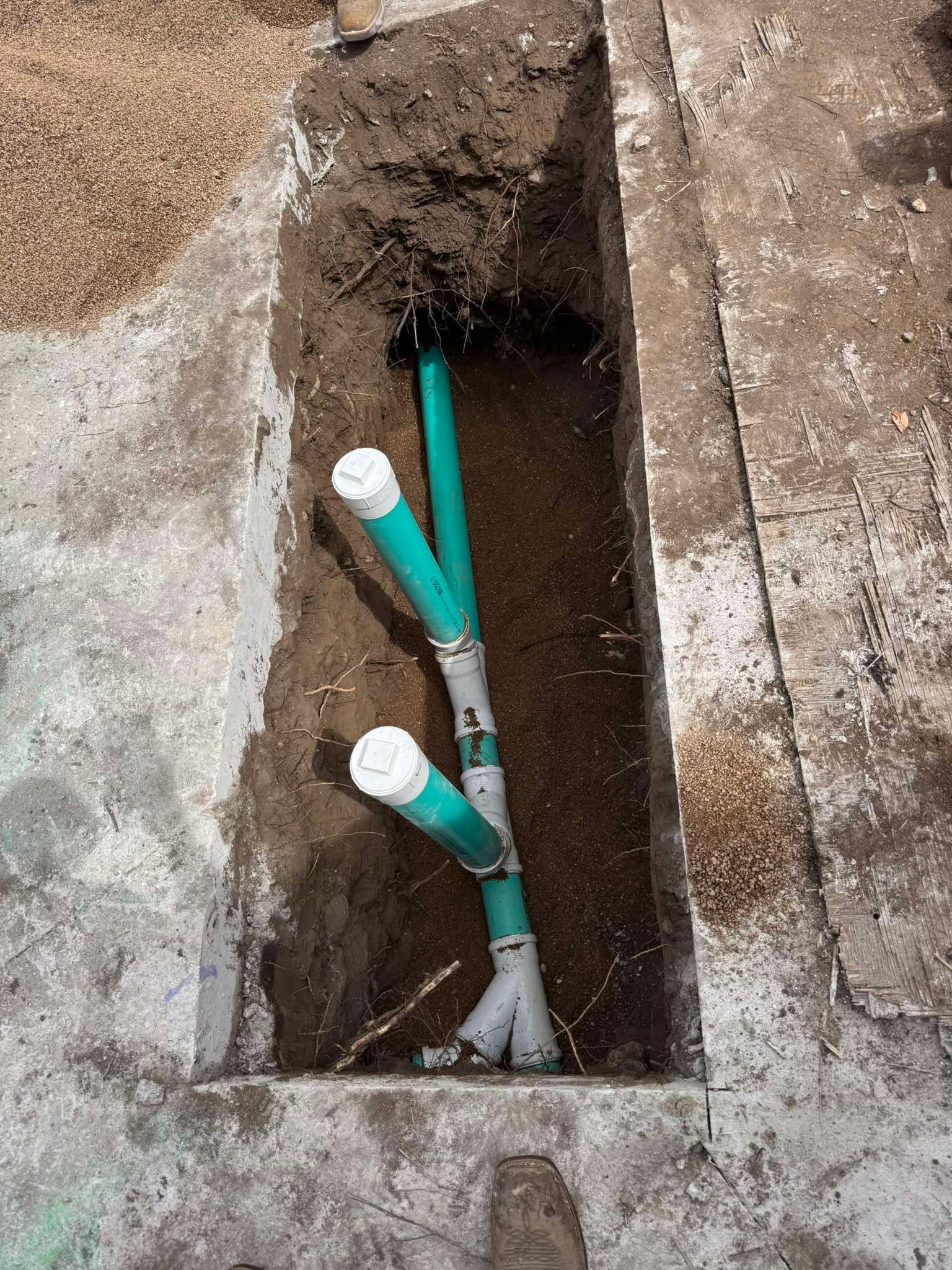 Green PVC plumbing pipes with white caps installed in a narrow, rectangular trench cut into a concrete surface.