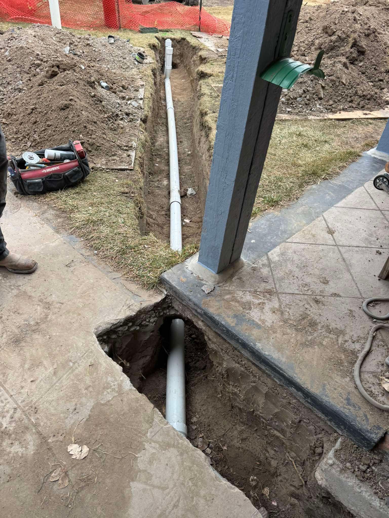 A trench with a PVC pipe installed in the ground alongside a concrete porch and lawn.