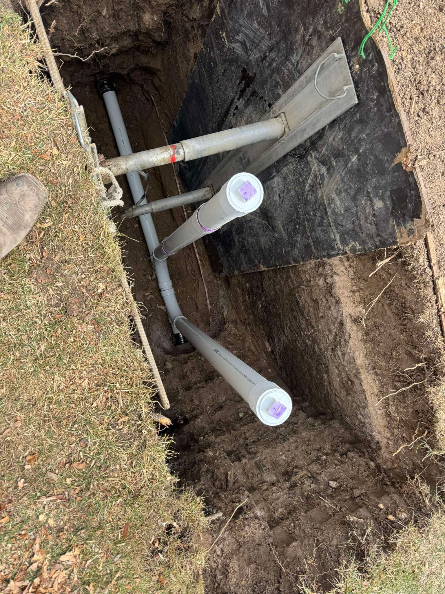 A rectangular trench in the ground containing several grey PVC pipes, two of which are capped and extending upward.