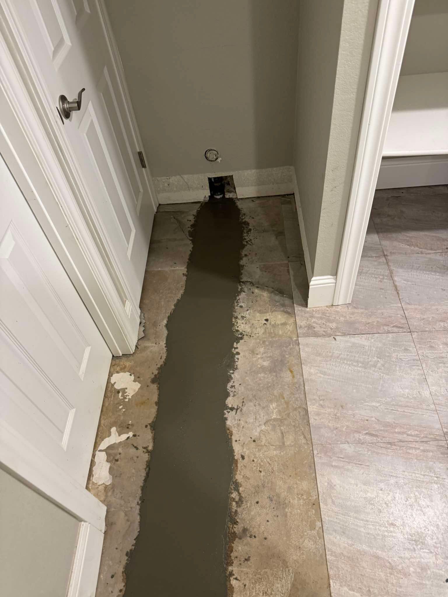 A long, dark concrete trench filled in on a beige tiled floor inside a hallway, leading toward an open wall cavity.
