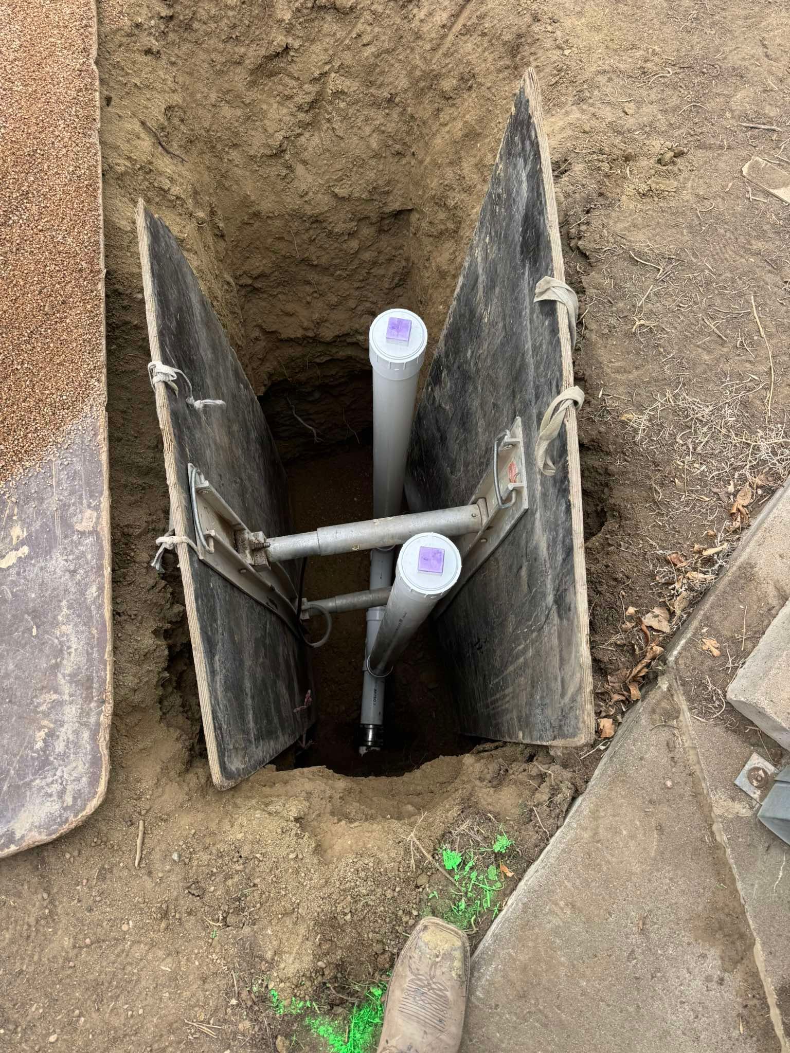 Two vertical grey PVC pipes installed in a trench braced by metal plates for stability.
