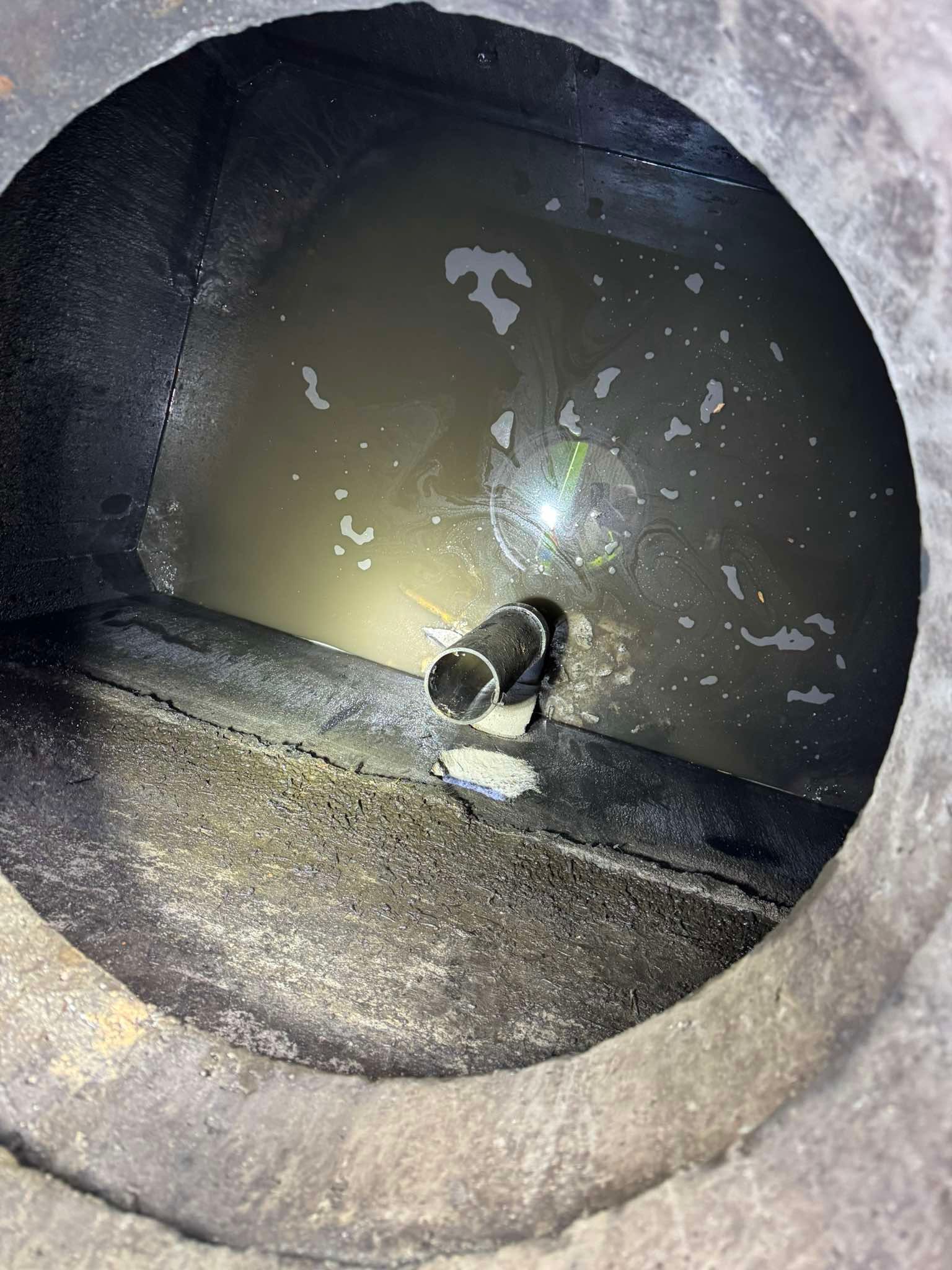 An interior view looking down into a dark, cylindrical tank containing murky water and a central metal pipe fitting.