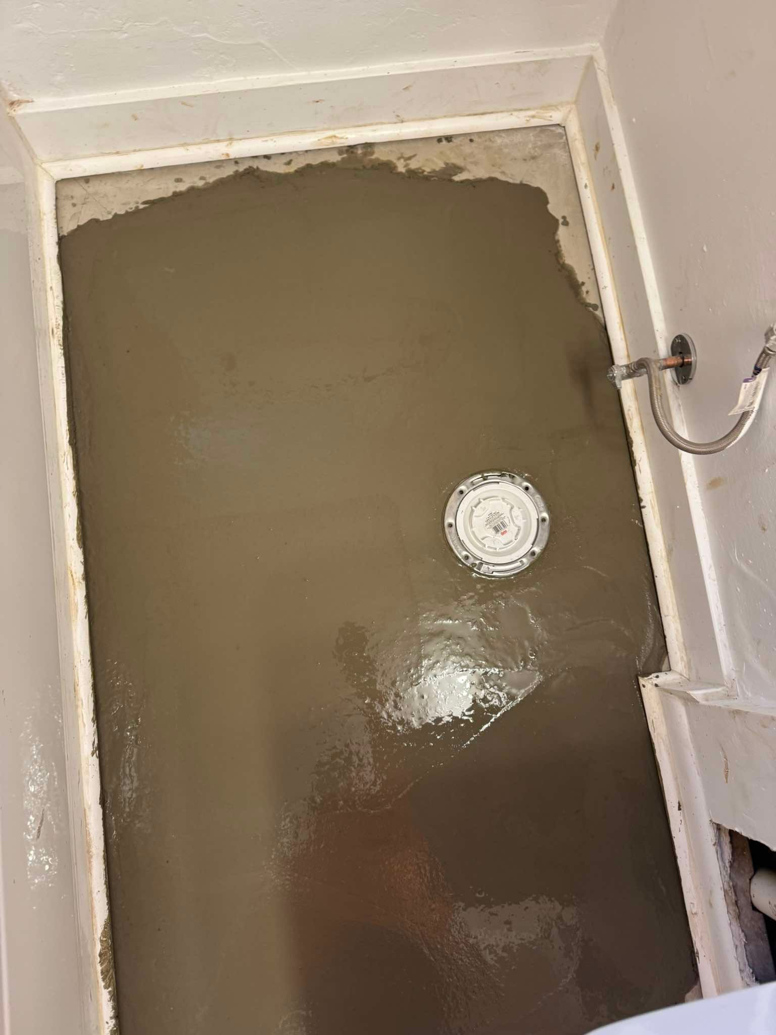 A view looking down at a bathroom floor covered in fresh, wet, gray concrete with a centered circular shower drain flange.