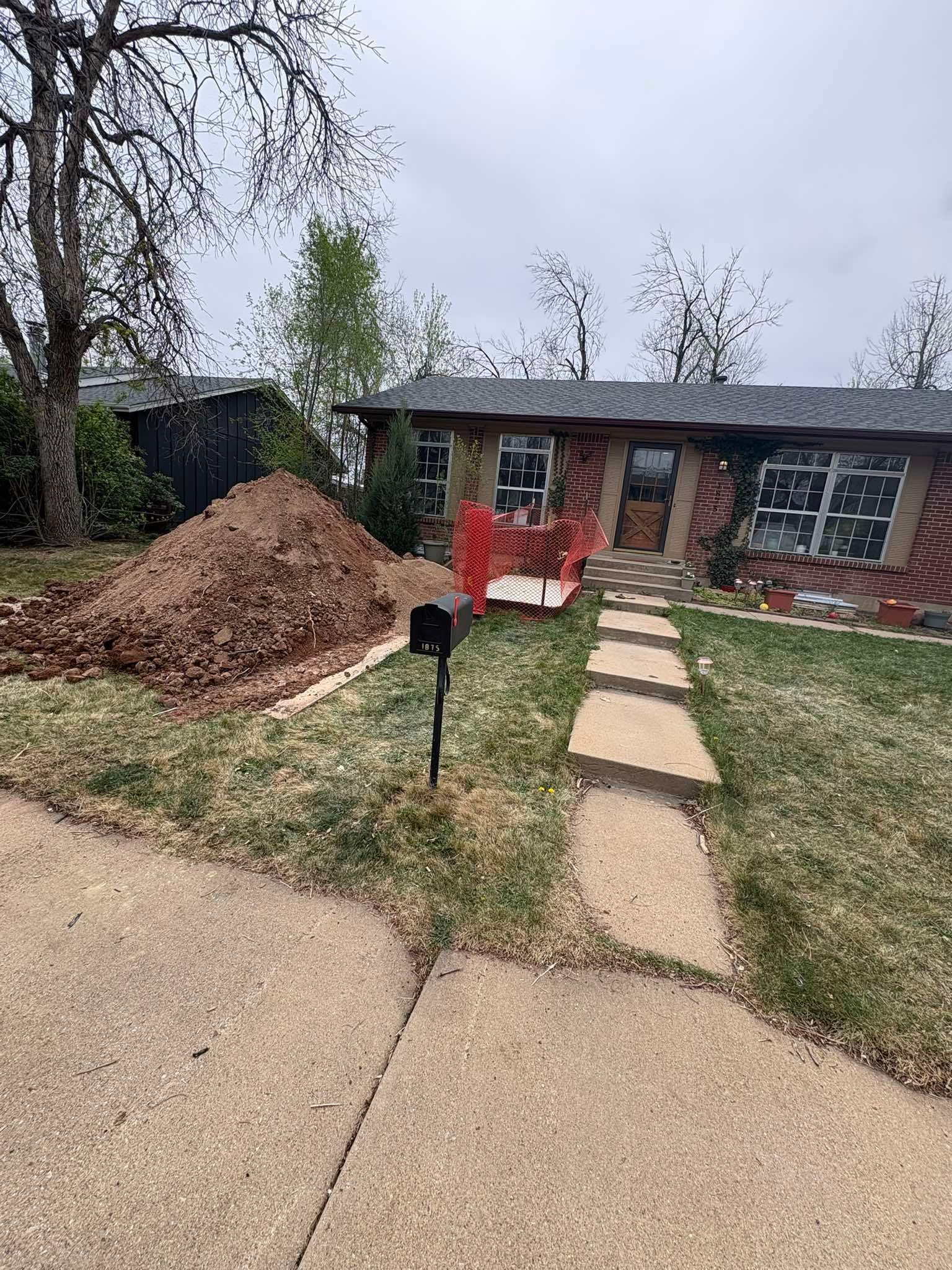 A brick house with a front walkway, a mailbox, and a large pile of brown leaves on the front lawn.