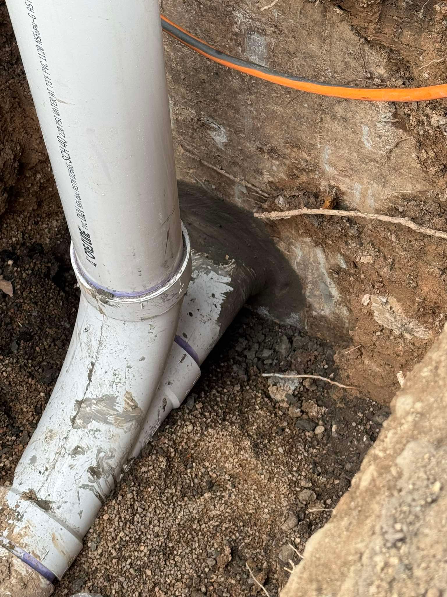 A white PVC drainage pipe curves into the ground, connecting to a dark pipe buried in the soil.