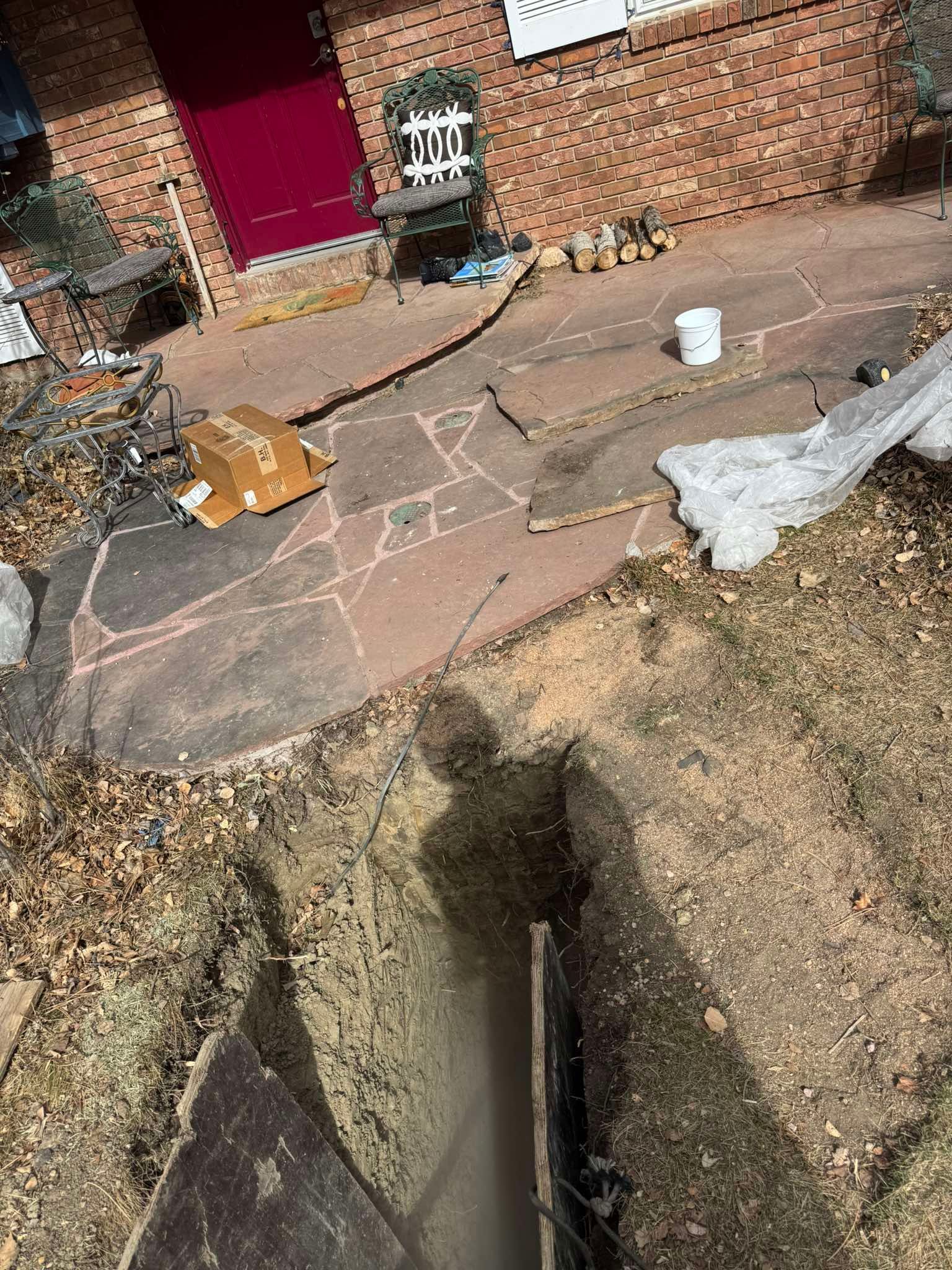 A flagstone patio featuring a brown cardboard box, a white bucket, and scattered packing materials near a red front door.