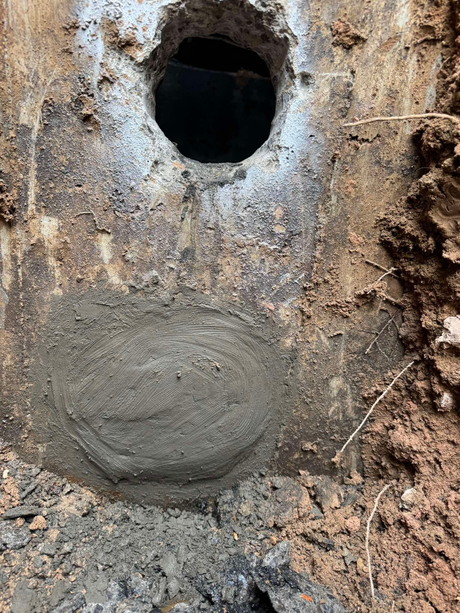 A concrete surface with an open circular hole above a circular patch of fresh, damp gray mortar.
