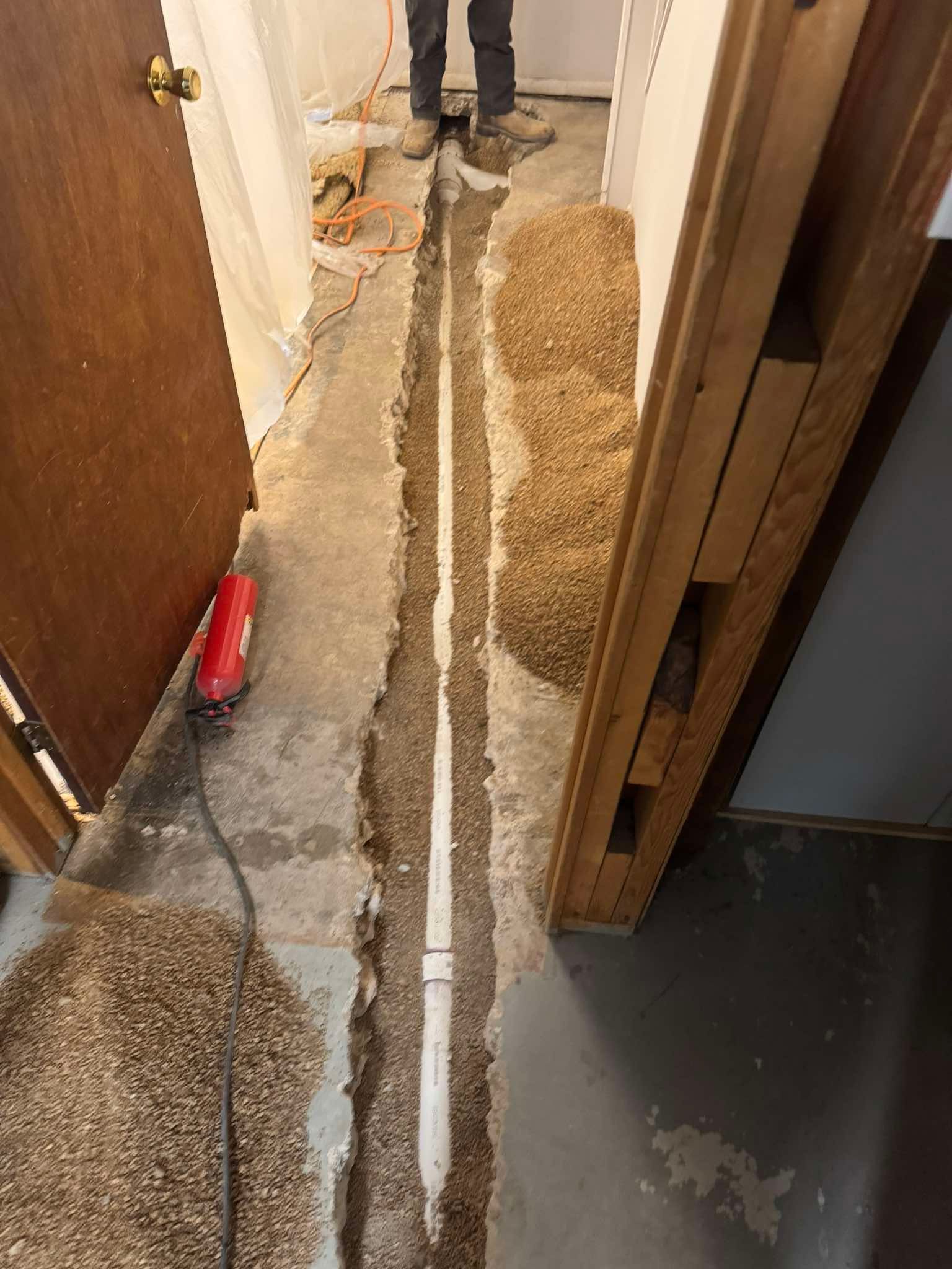 A narrow trench cut through a concrete floor reveals a newly installed white PVC pipe centered in the ground.