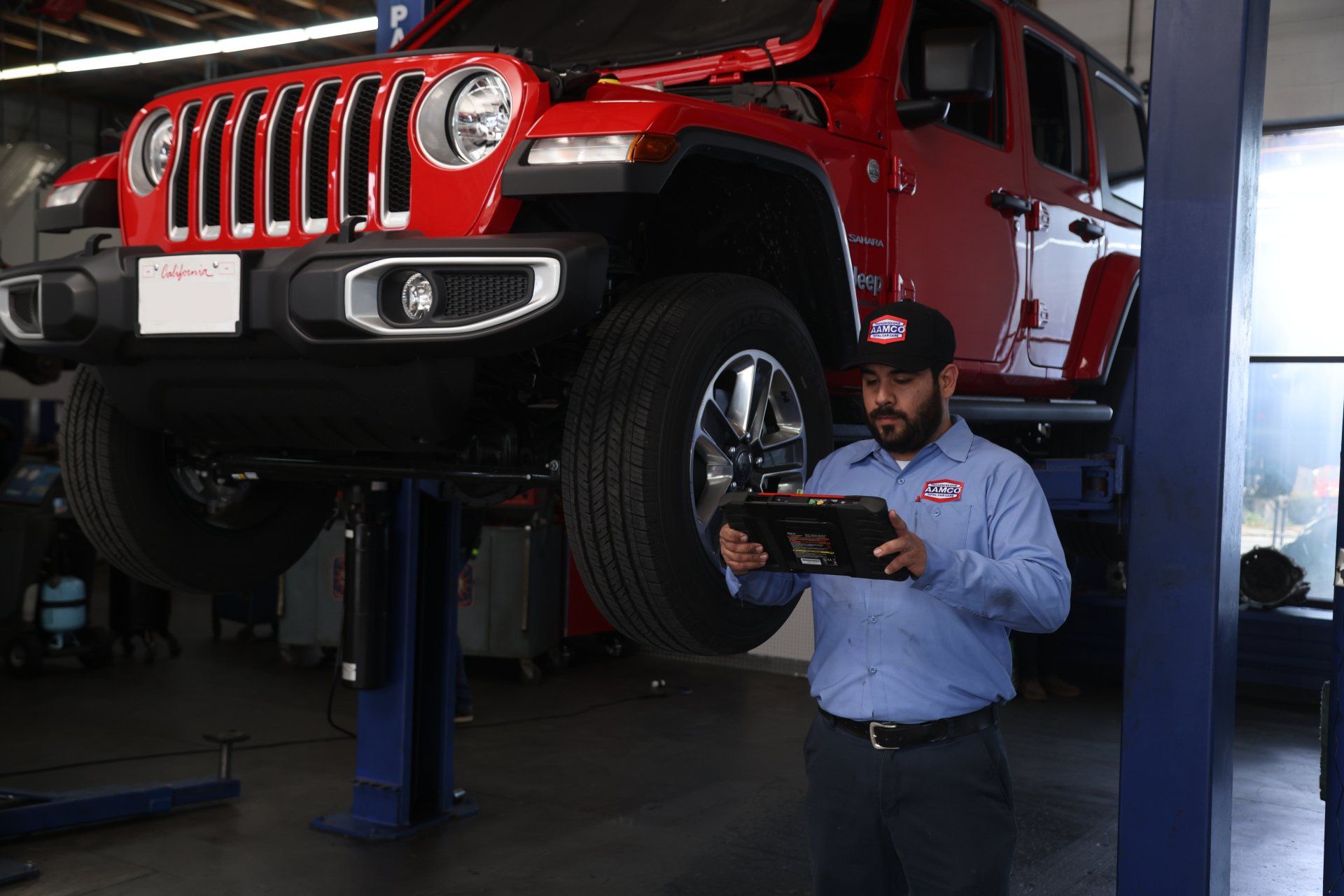 A man is looking at a tablet in front of a red jeep on a lift.