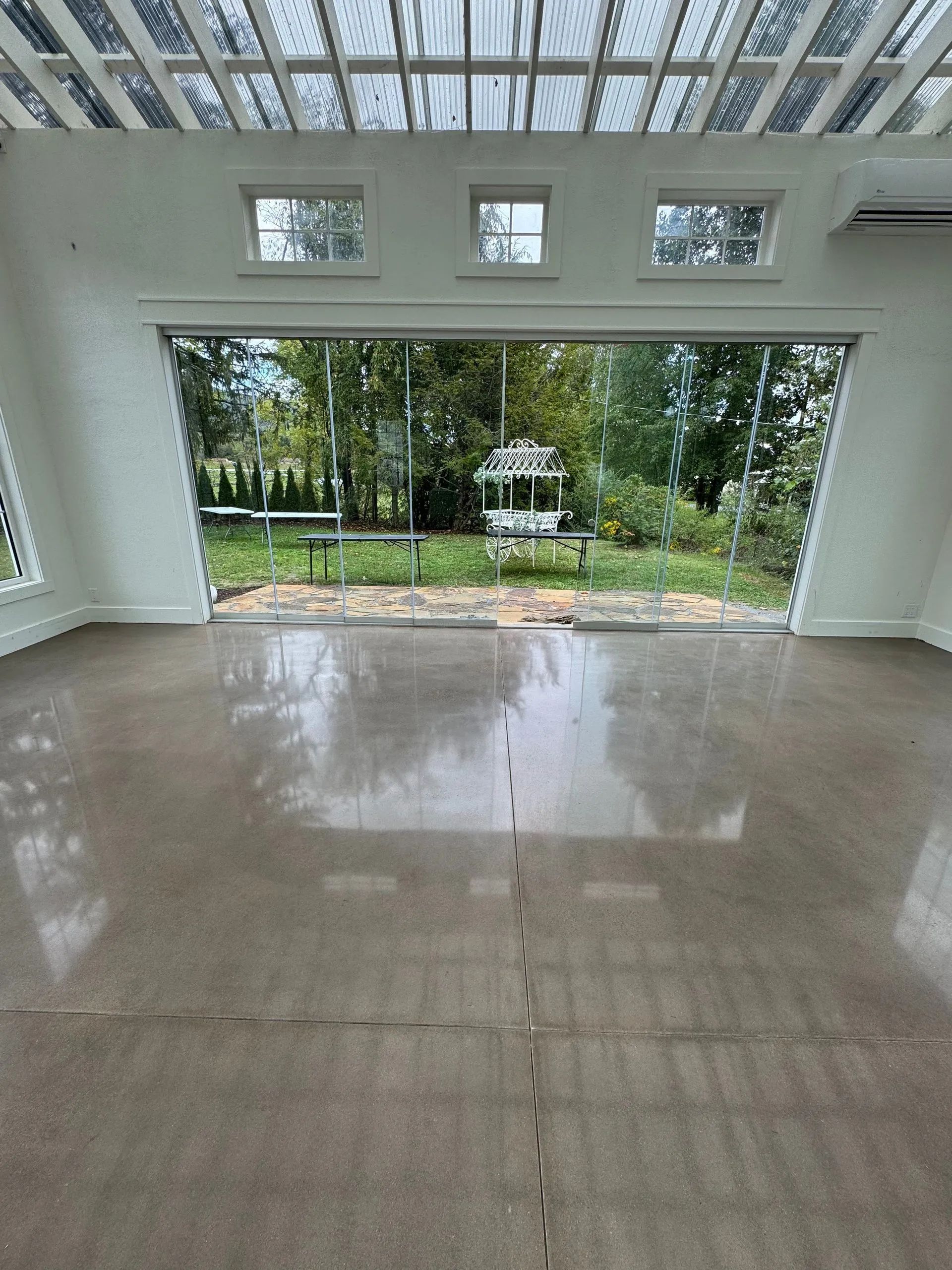 Empty white room with glossy floor, large open doorway, and a view of trees and garden outside