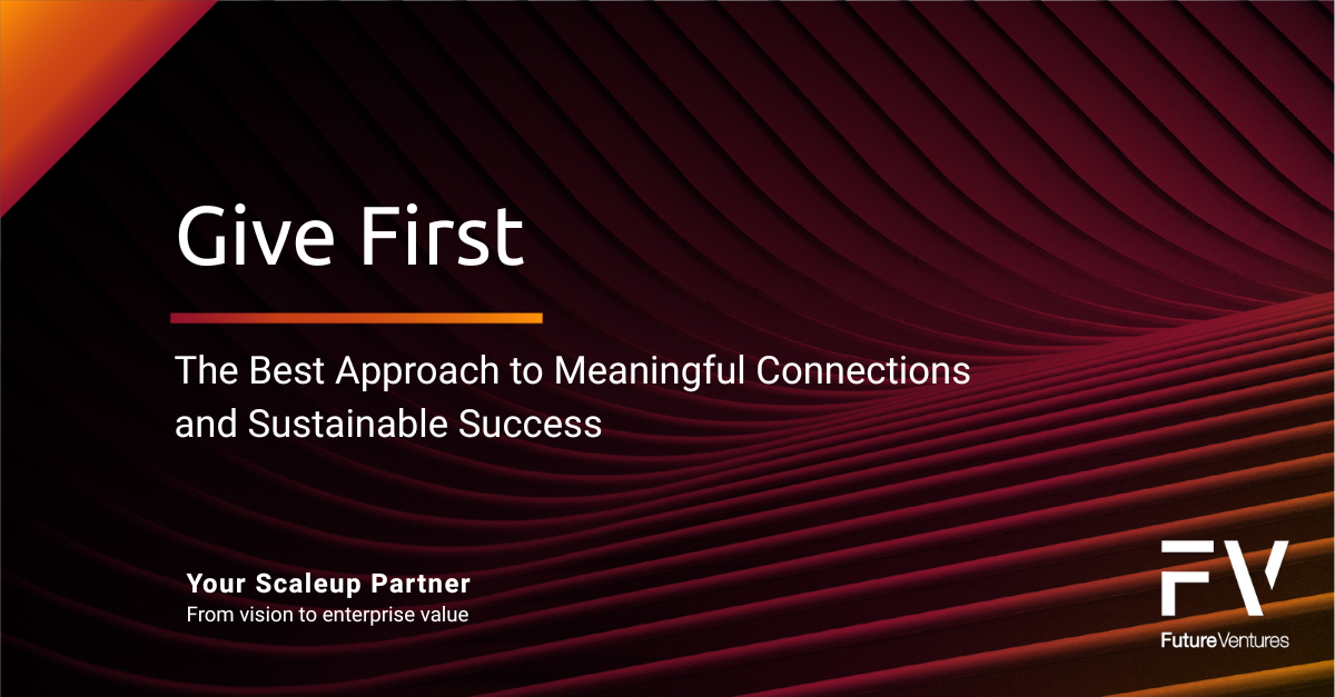 People around a table with laptops, laughing. Bookshelves in the background.