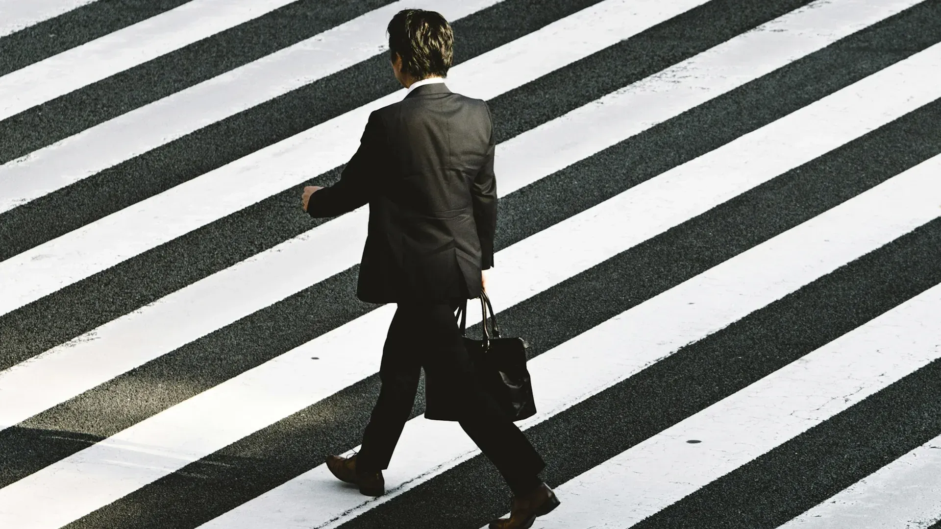 Man in a suit crossing a diagonal crosswalk, carrying a briefcase.