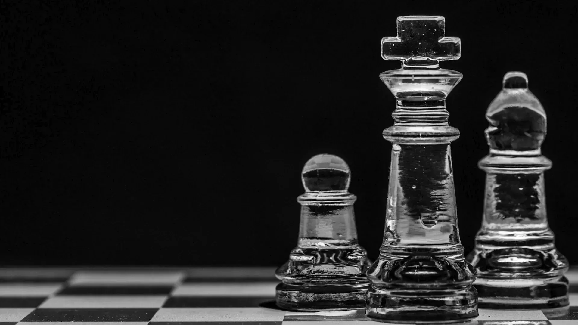 A black and white photo of three glass chess pieces on a chess board.