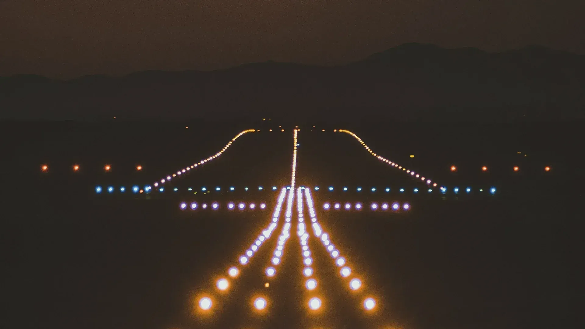 Runway at night, lit with bright white and yellow lights leading to the distant horizon.