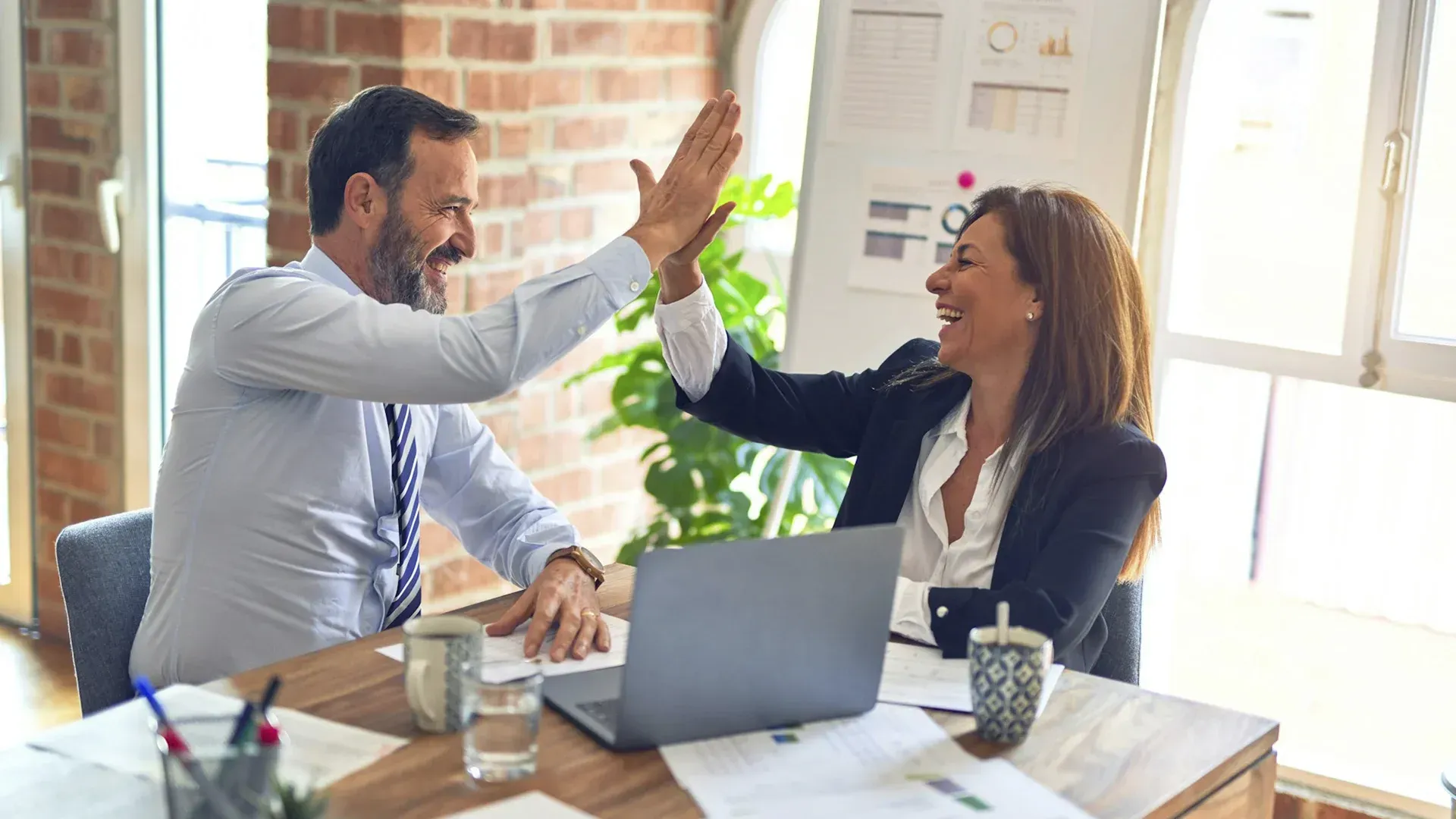 Man and woman high-fiving at a desk in an office, smiling.