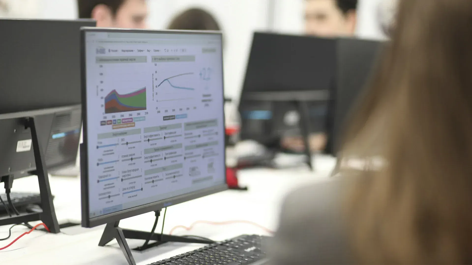 A woman sits in front of a computer monitor displaying a graph.