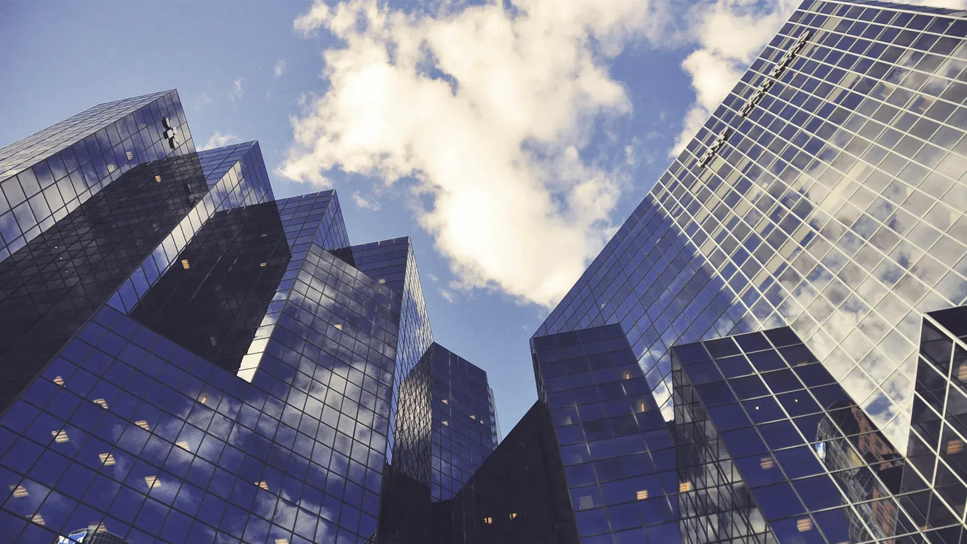 Skyscrapers reaching towards a blue sky with fluffy white clouds; looking upwards.