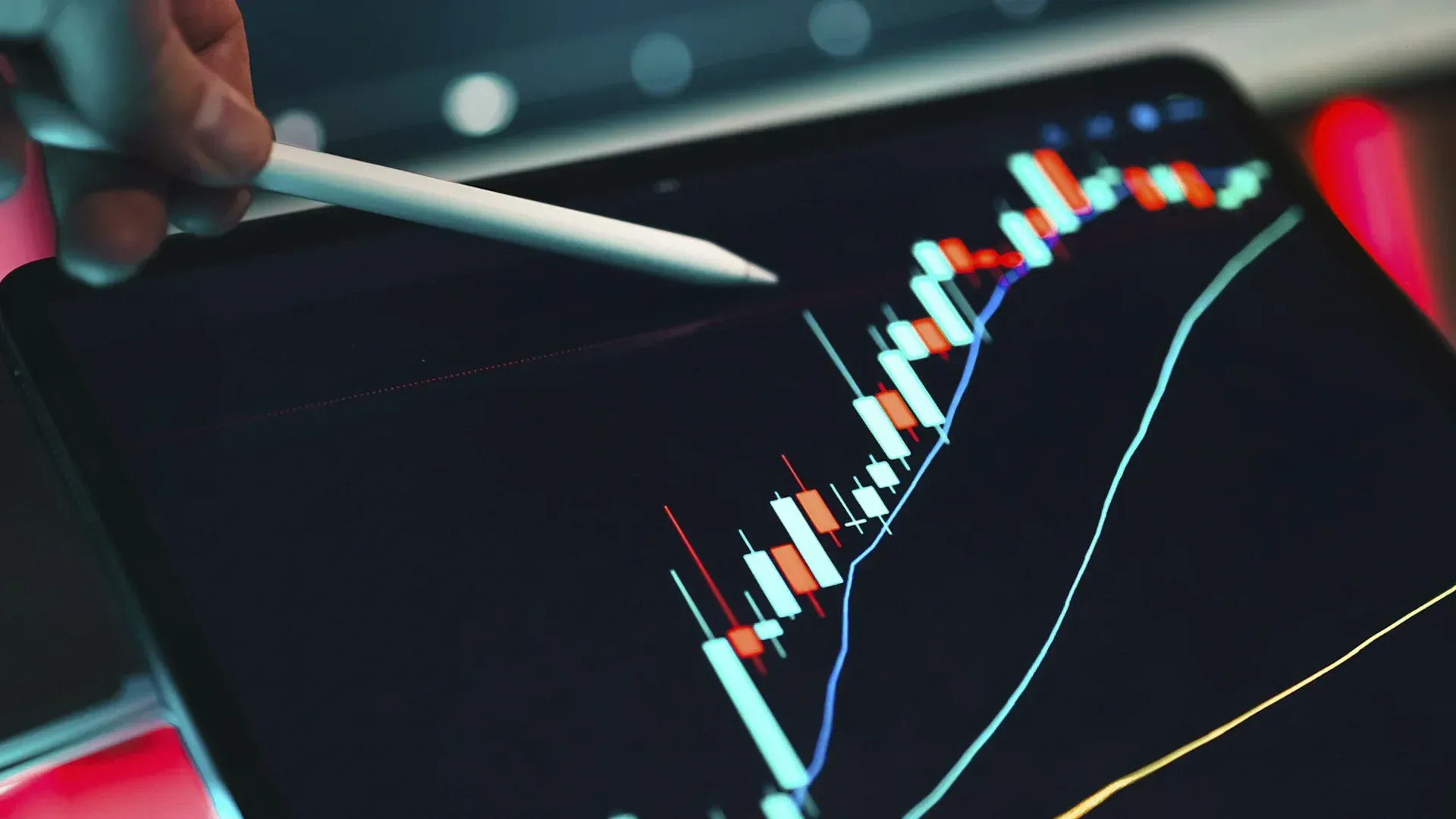 Person uses a stylus to analyze a stock chart on a tablet. Blue and red lines show fluctuating market trends.